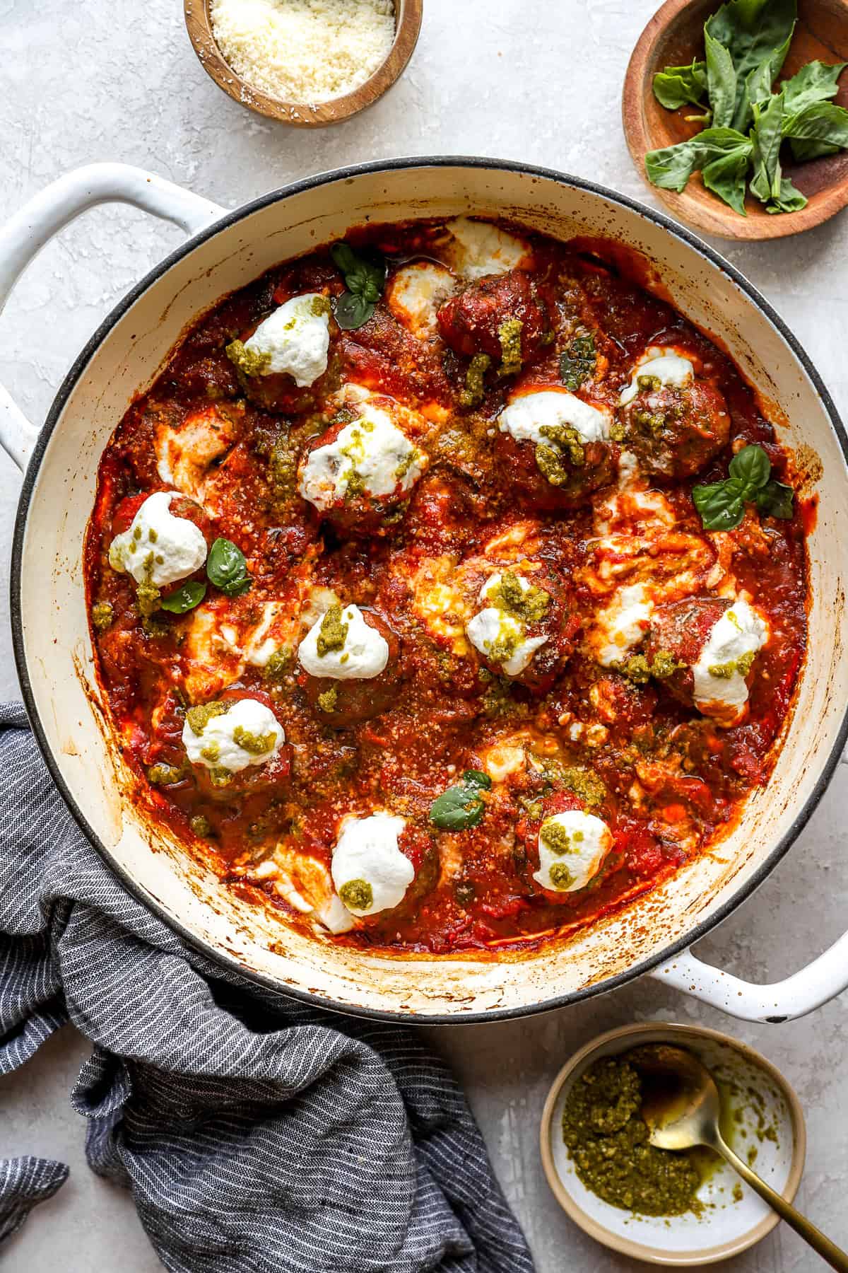 Pizza meatballs topped with ricotta and fresh herbs in a skillet. 