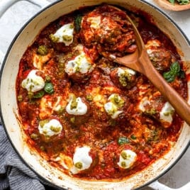 A wooden spoon scooping a pizza meatball from a skillet.