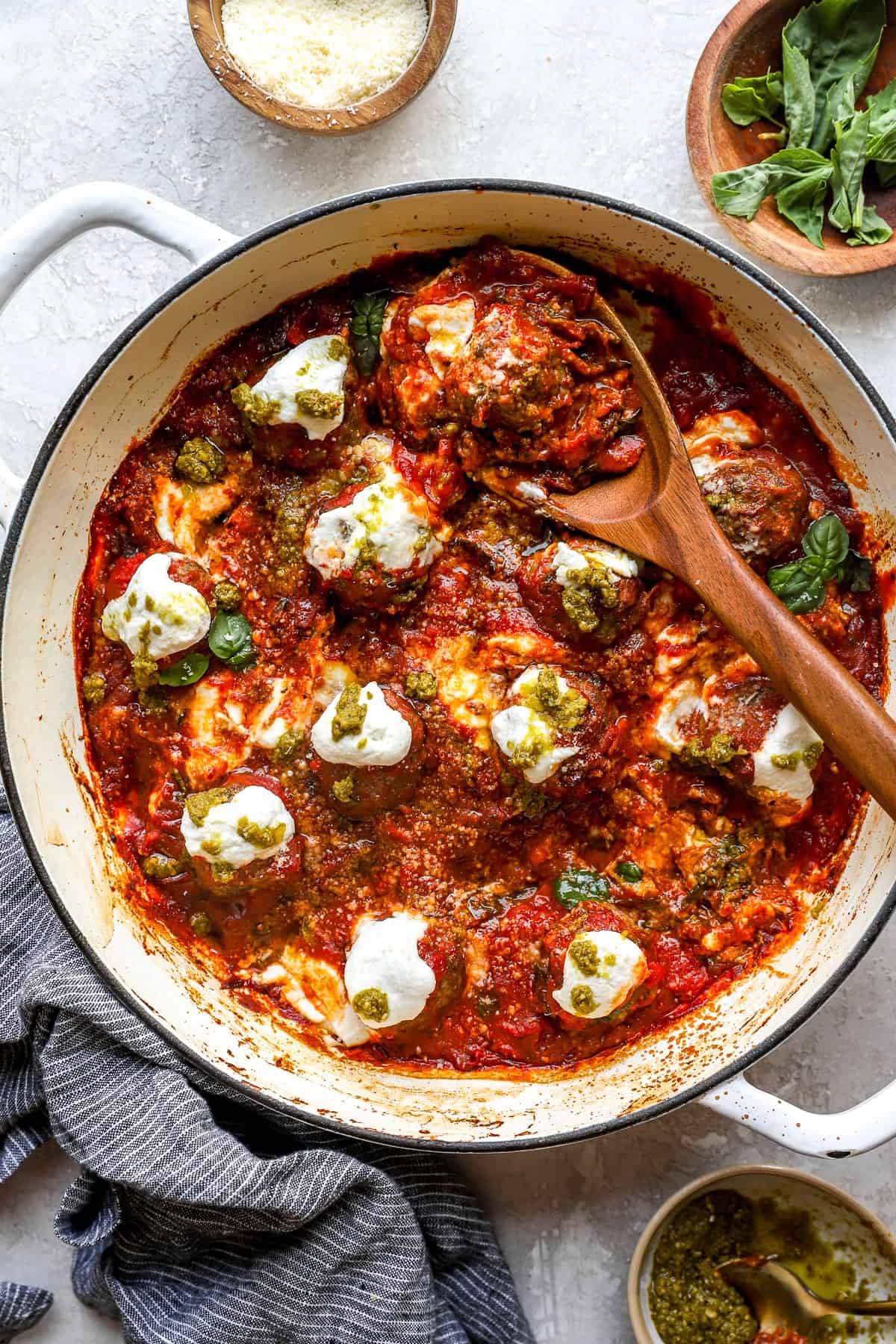 A wooden spoon scooping a pizza meatball from a skillet. 