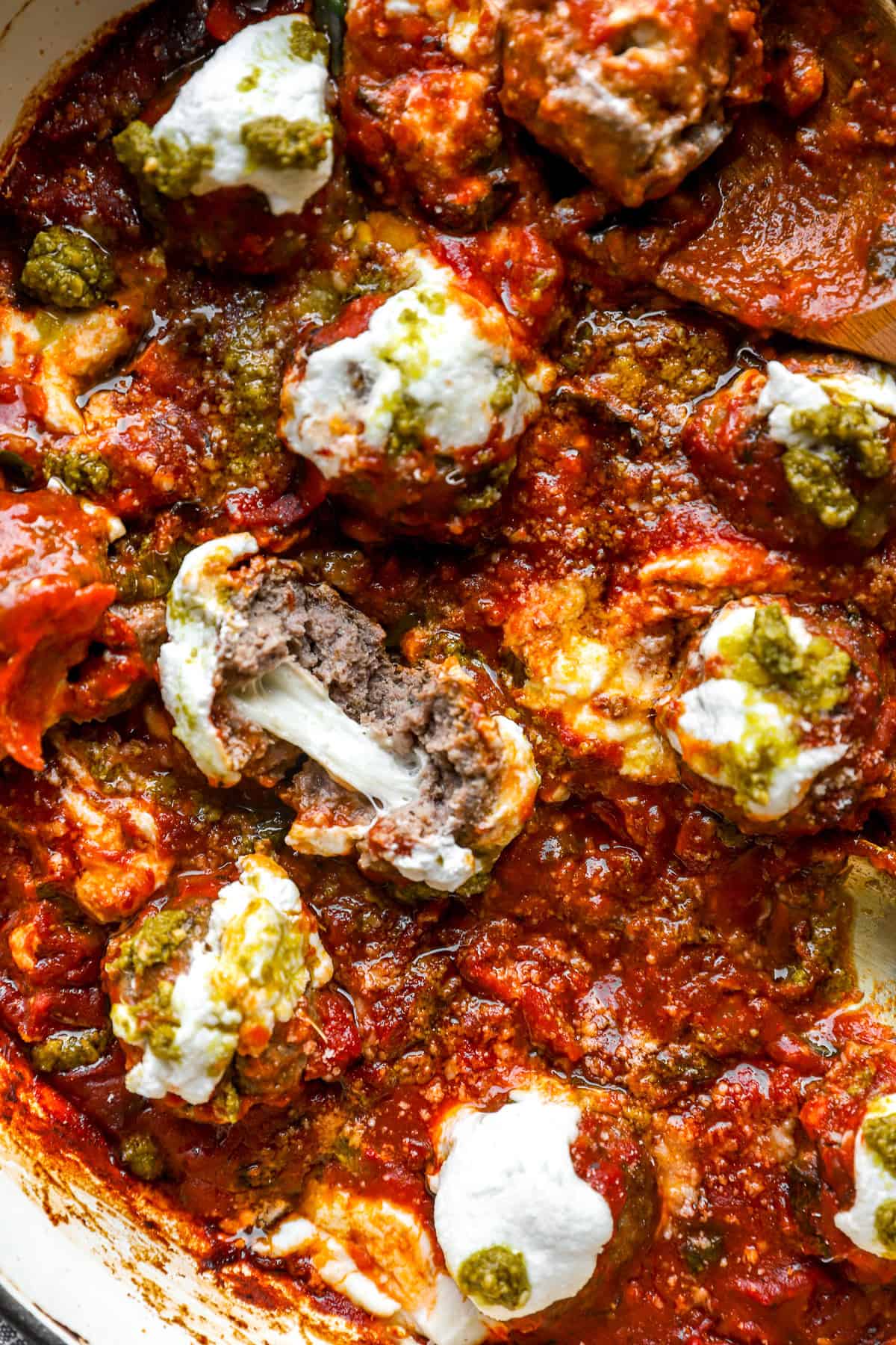 Pizza meatballs in a skillet, one split in half exposing the cheesy center. 