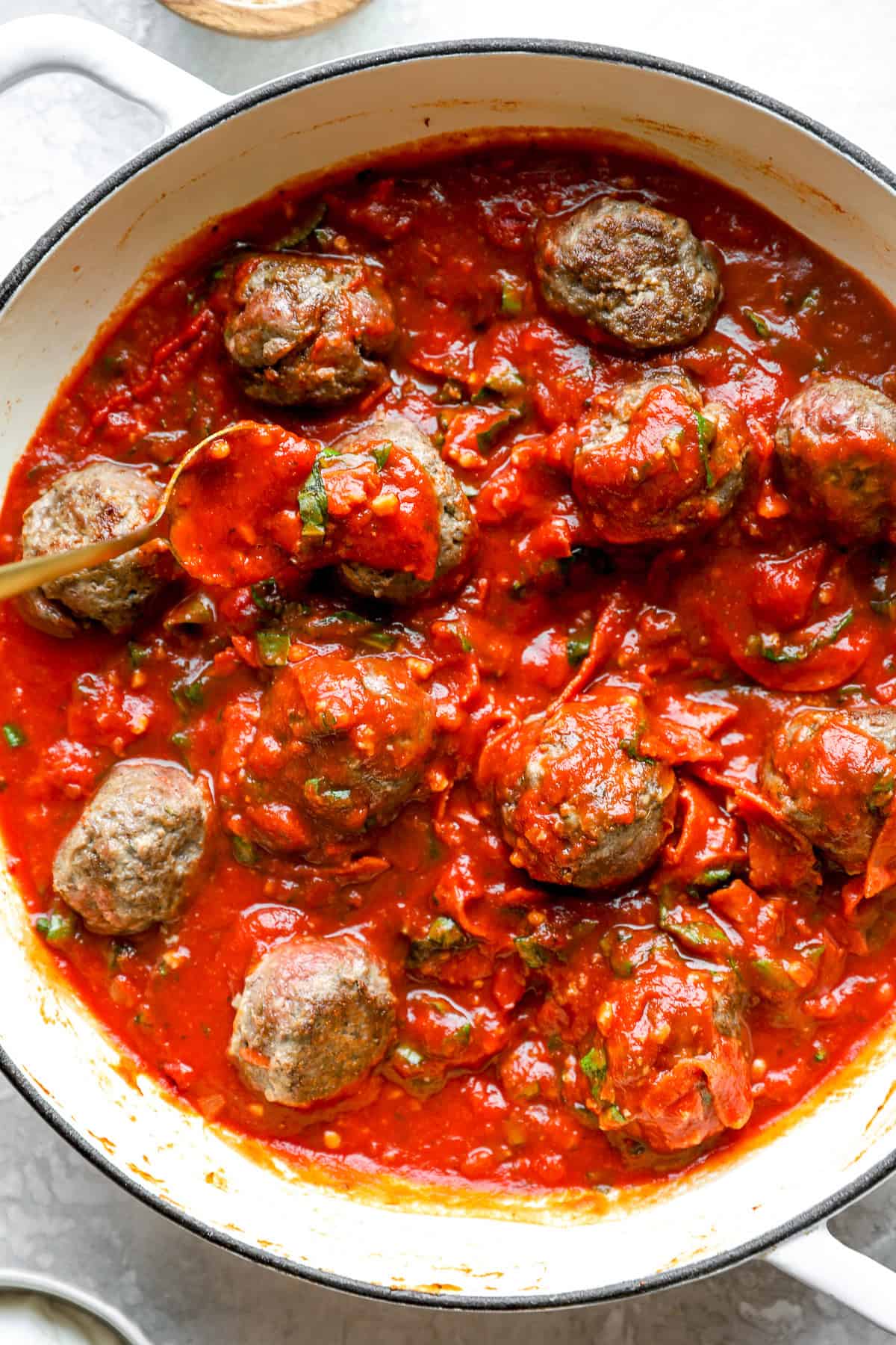 Seared meatballs being added to a pot of marinara sauce. 
