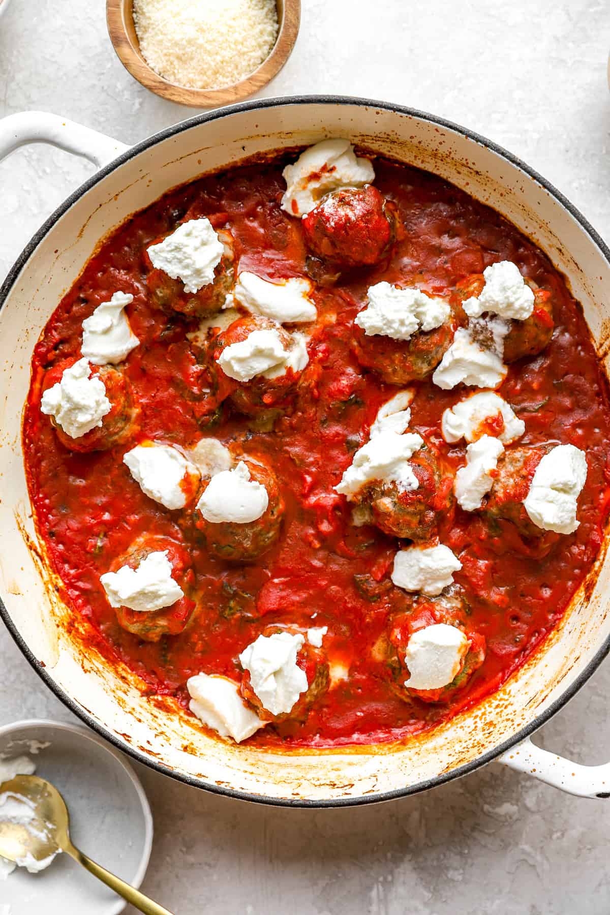 Ricotta cheese on top of pizza meatballs in a skillet. 