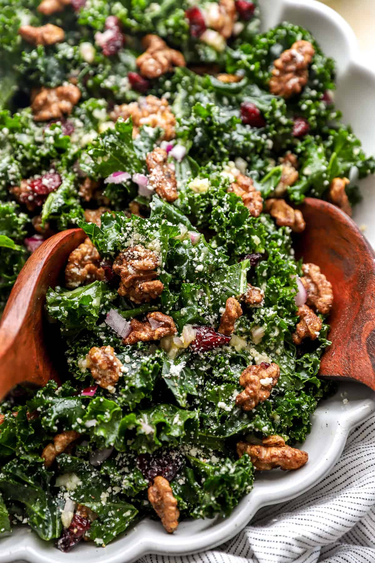 A fall kale salad with candied pecans, red onion, cheese, and shallot vinaigrette with two wooden serving spoons on top. 