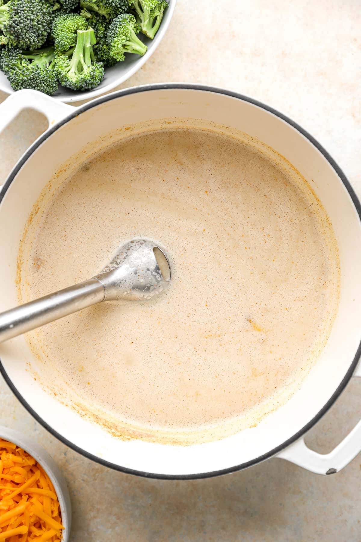 Broccoli cheddar soup being blended with an immersion blender. 