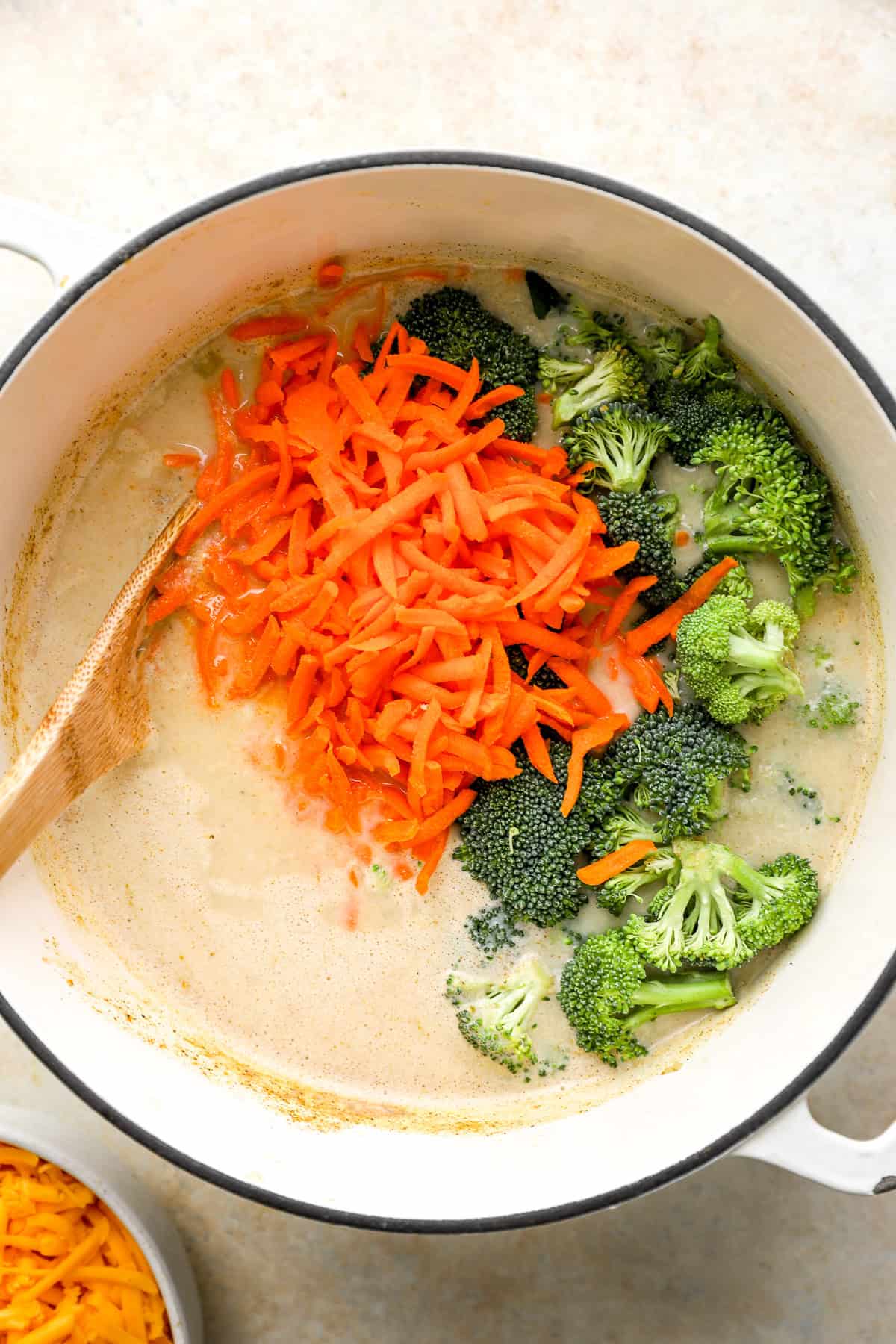 Broccoli and shredded carrots being added to a pot of broccoli cheddar soup. 