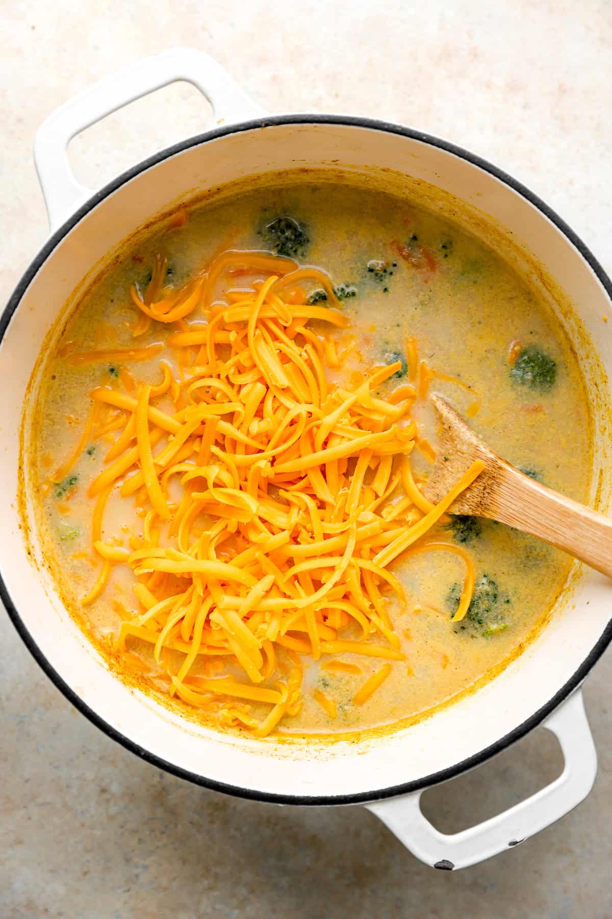 Shredded cheddar being added to a pot of broccoli cheddar soup. 