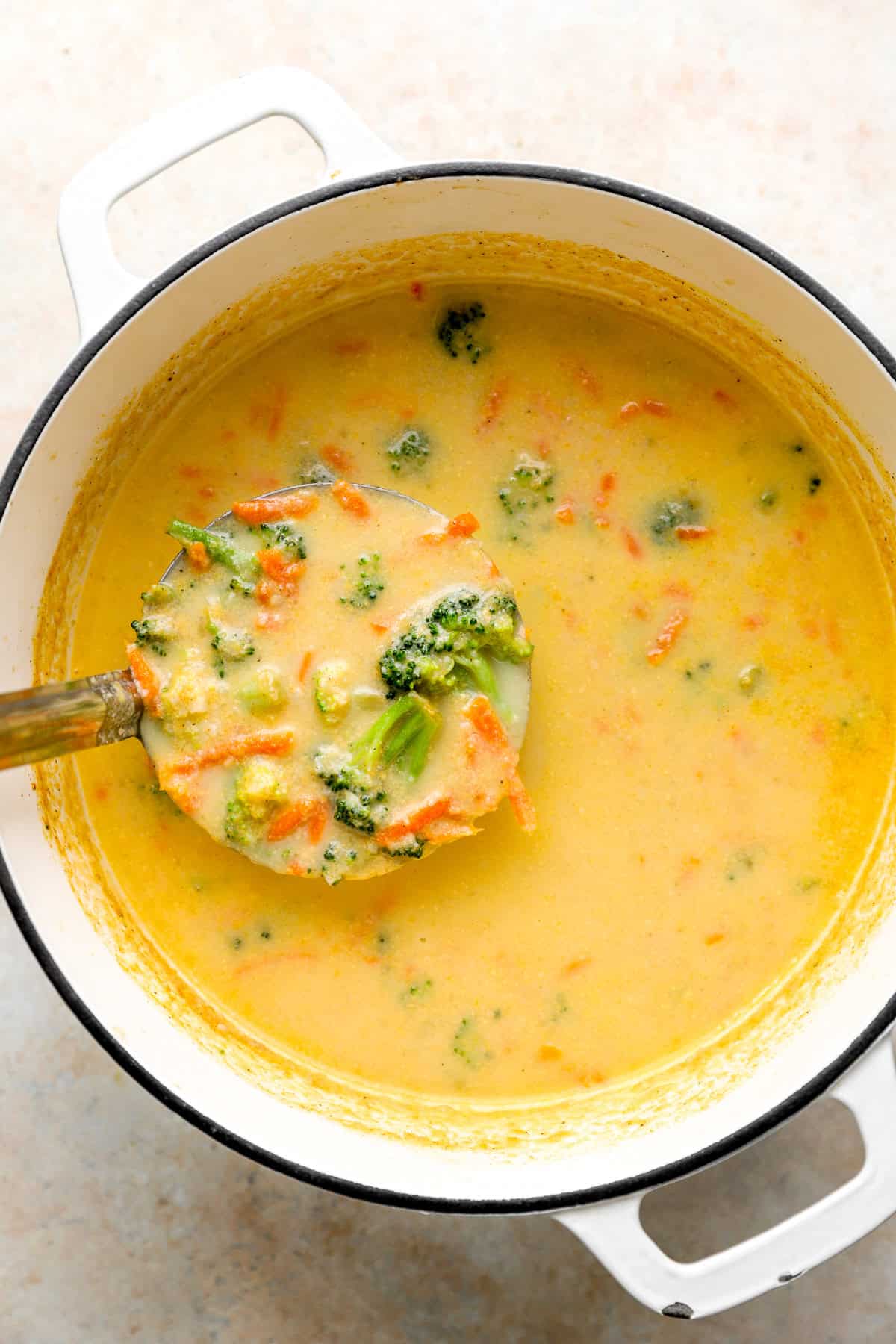 A ladle of healthy broccoli cheddar soup being lifted from a pot.