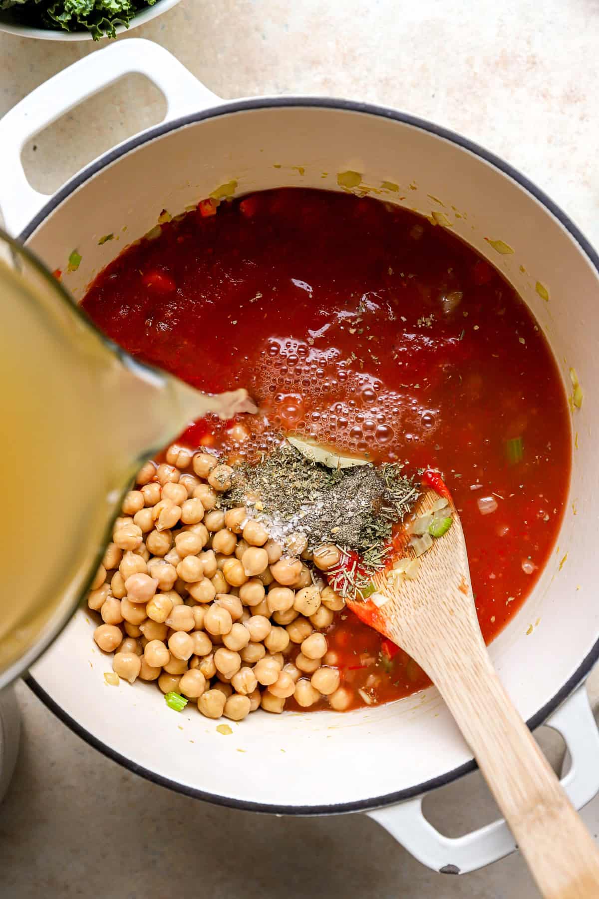 Chickpeas, tomatoes, seasonings, and broth being added to a pot of soup. 