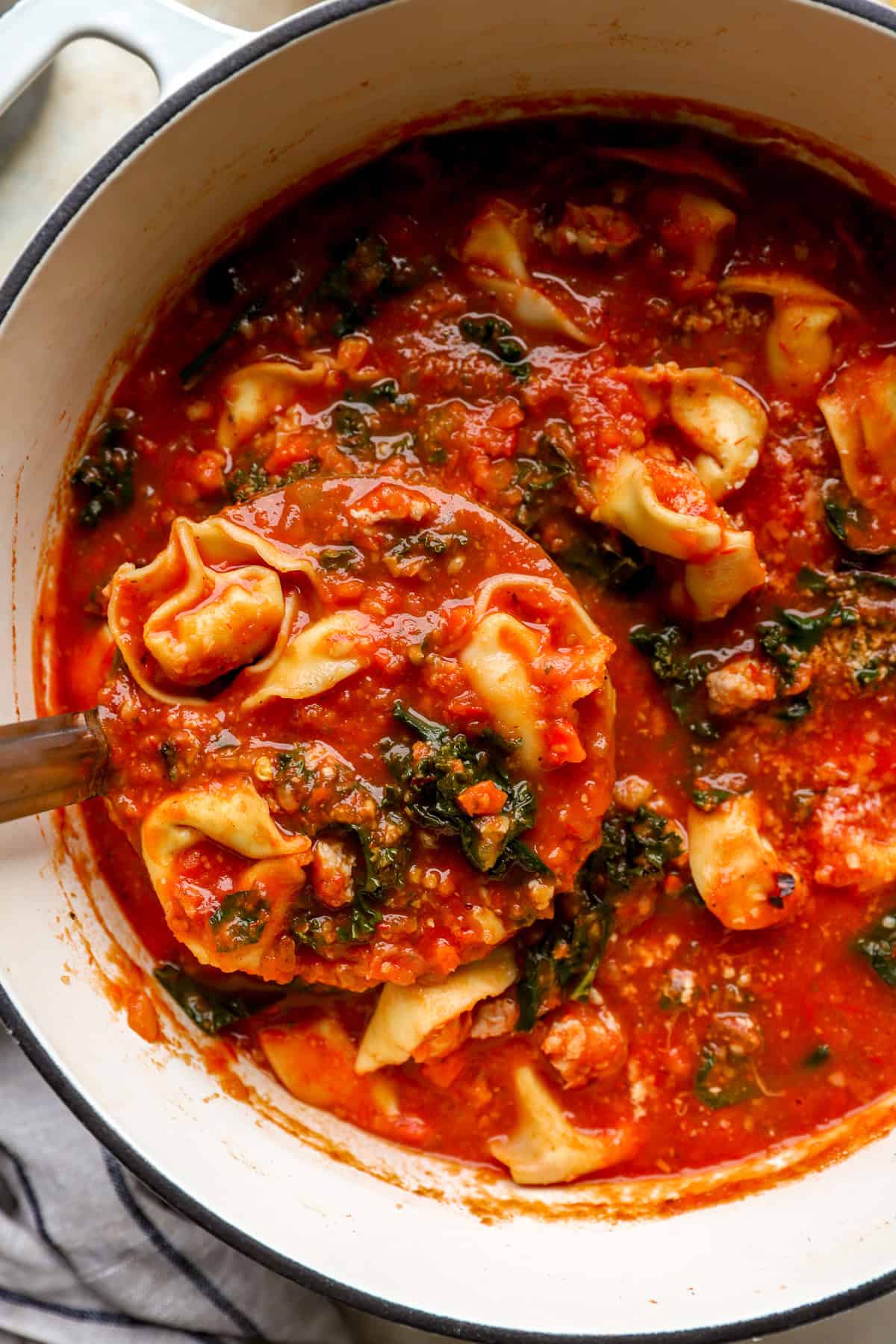 A ladle lifting tortellini soup from a pot.