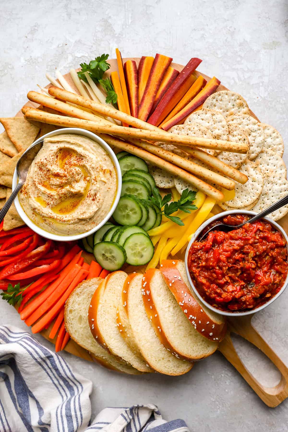 A platter of fresh veggies, breadsticks, bread, crackers, hummus, and matbucha.