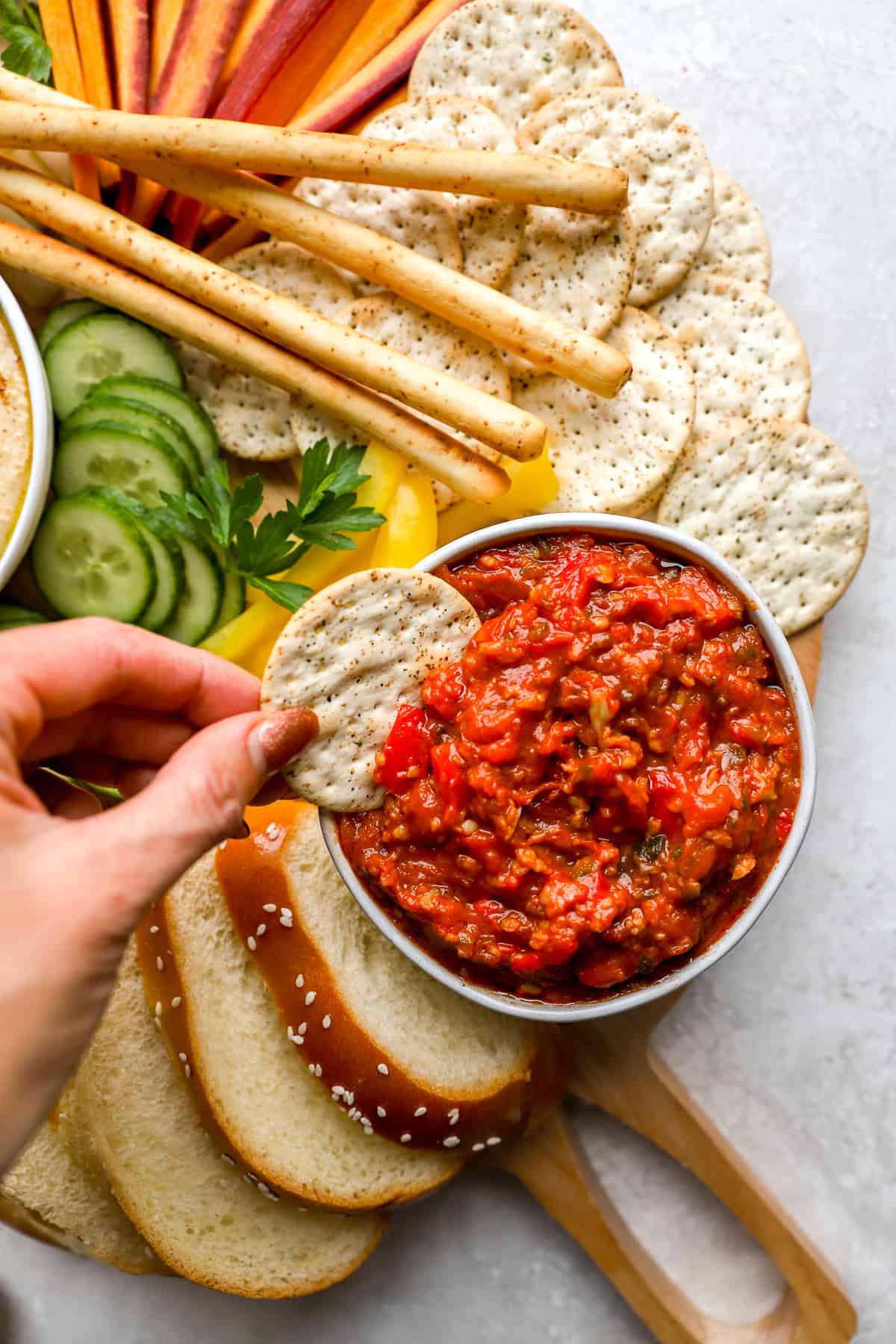 A cracker being dipped into a bowl of matbucha. 