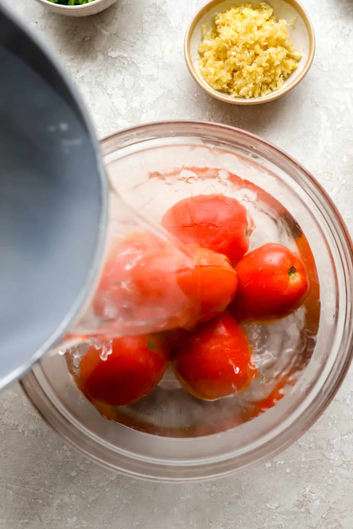 Boiling water being poured over a bowl of tomatoes.