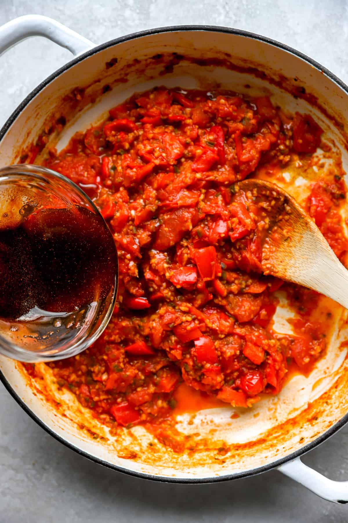 An olive oil mixture being poured into a skillet of matbucha. 