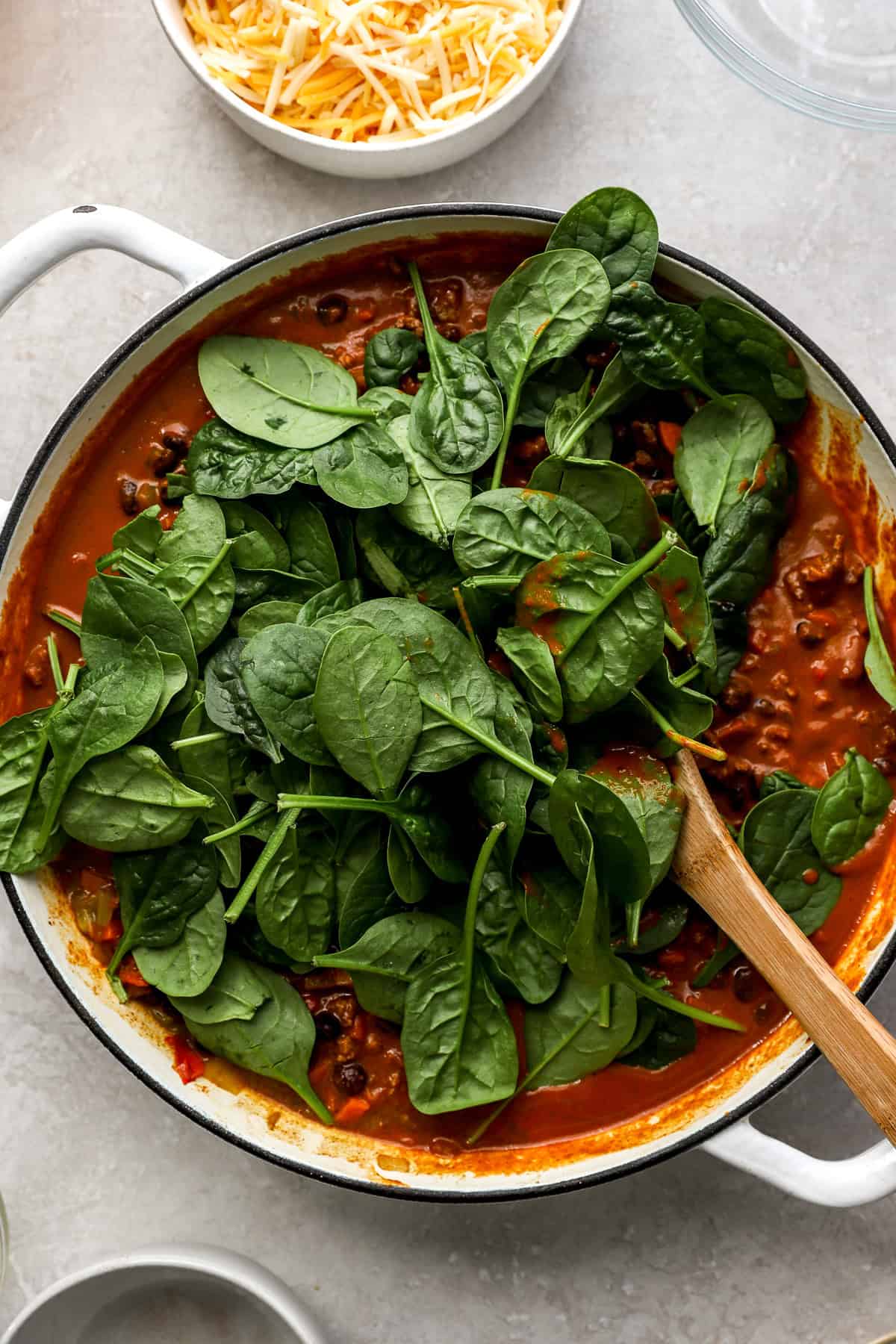 Spinach being stirred into a skillet of beef enchiladas. 
