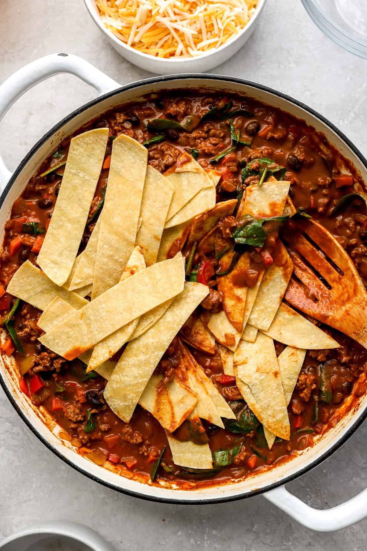 Tortilla strips being folded into a pan of beef enchiladas. 
