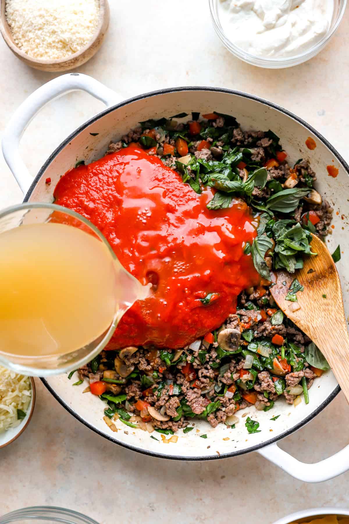 Broth and marinara sauce being added to a skillet of beef and veggies.