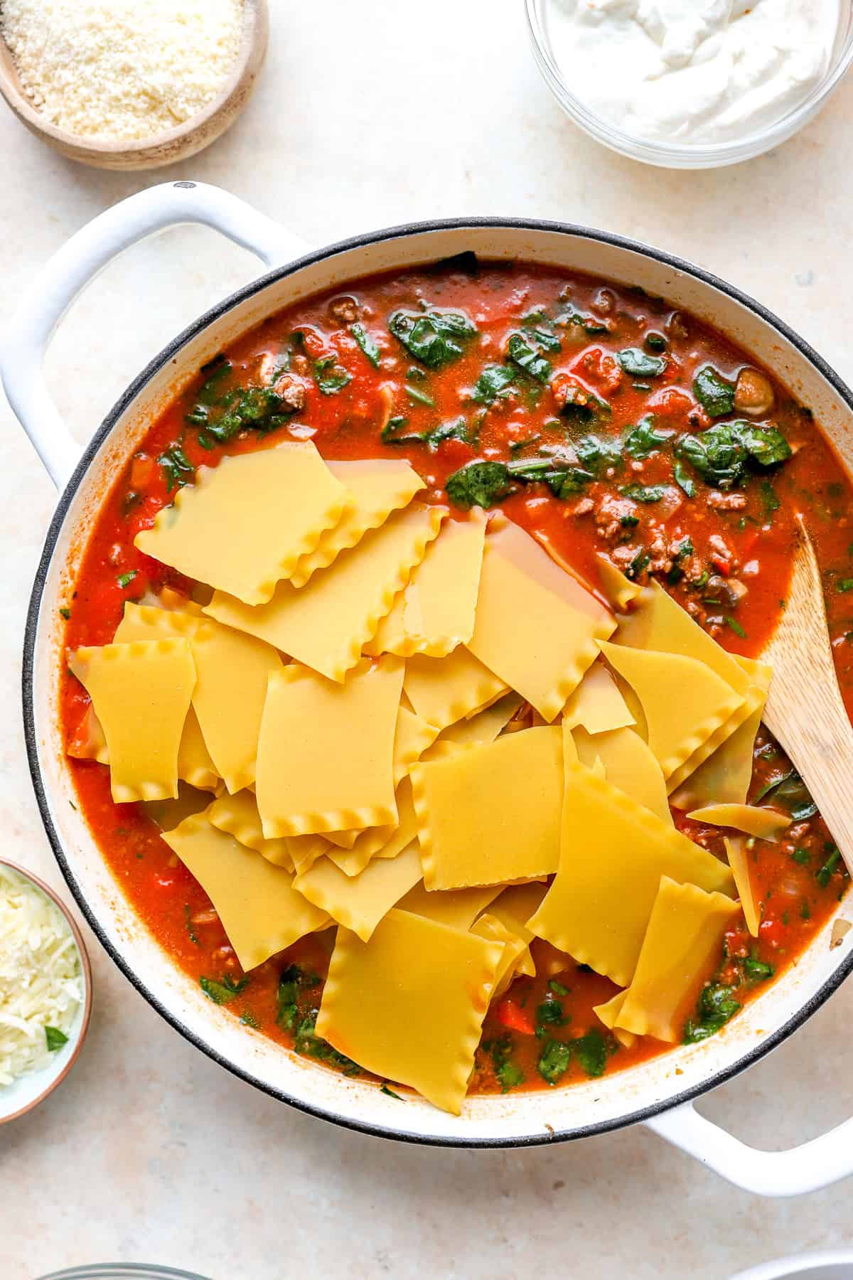 Lasagna noodles being added to a skillet of marinara sauce, beef, and veggies.