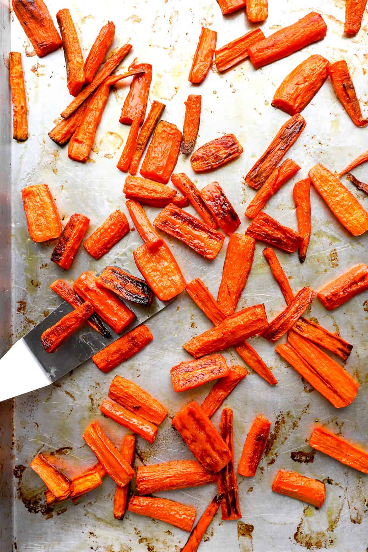 Roasted carrots being scooped from a rimmed baking sheet.