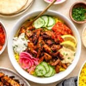 Chicken shawarma in a bowl with fresh veggies, hummus, and rice.