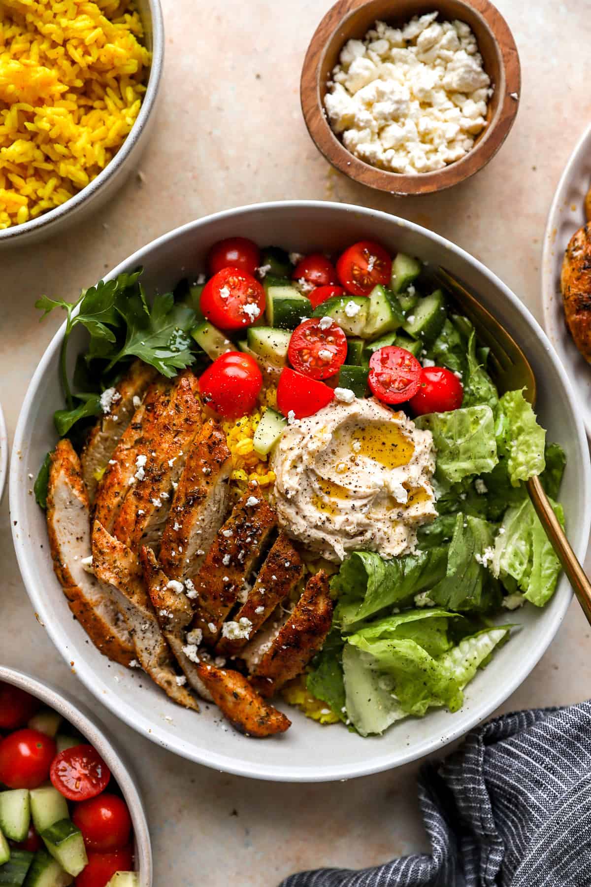 Sliced chicken cutlets on a salad with hummus, olive oil, and tomatoes.