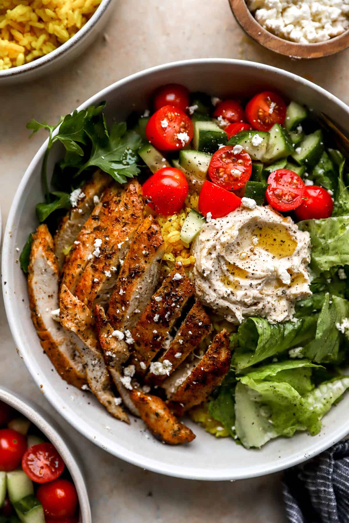 Sliced chicken cutlets on a salad with hummus, olive oil, and tomatoes.