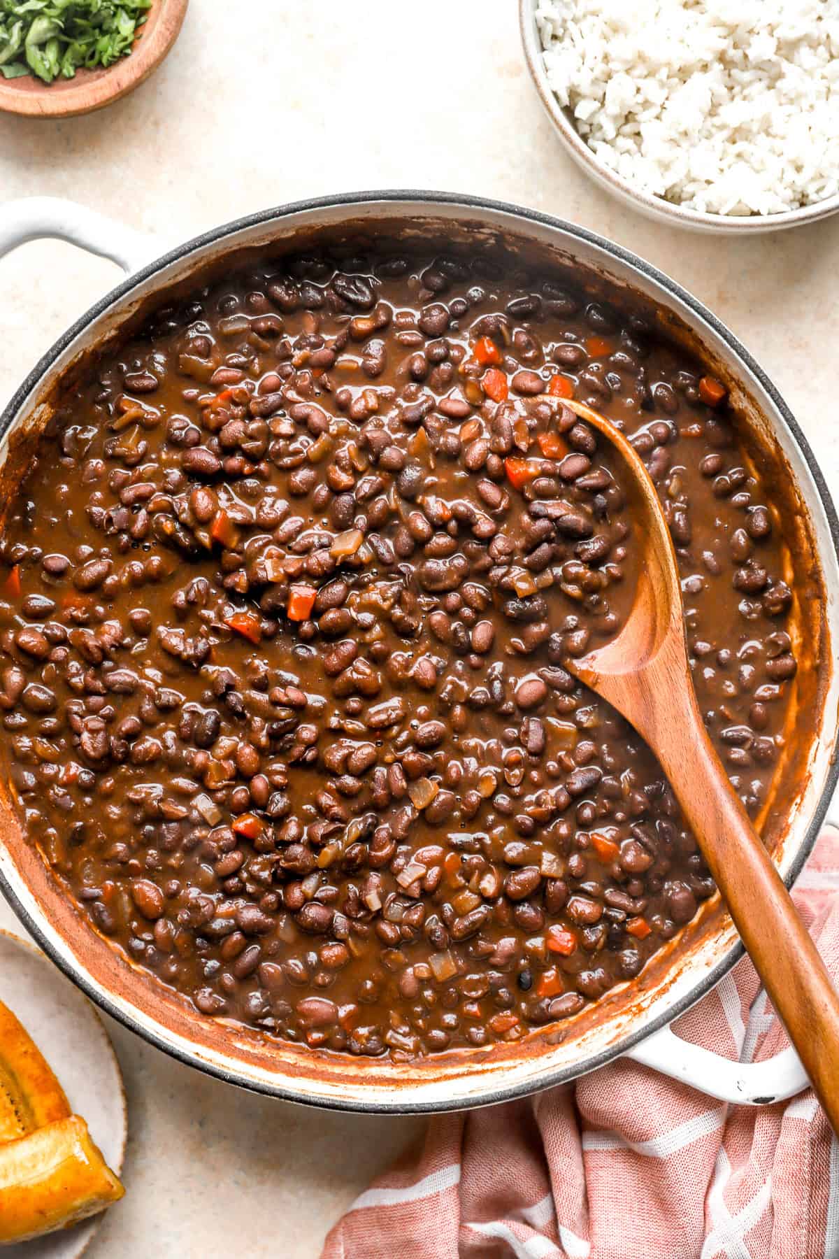 Costa Rican black beans in a skillet with a wooden spoon sticking out.