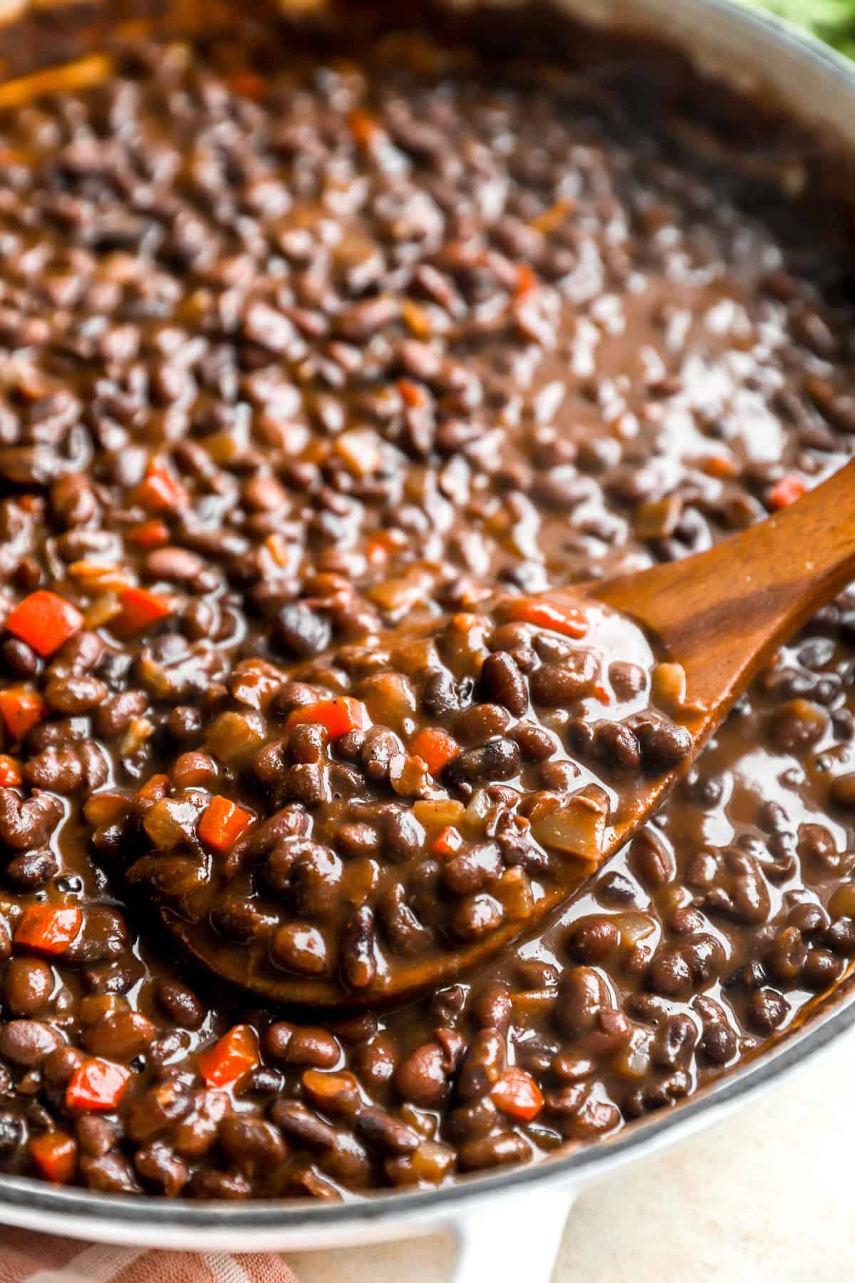 A wooden spoon lifting a scoop of Instant Pot black beans from a skillet. 