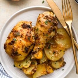 Garlic confit roasted chicken with potatoes on a plate, a knife and fork on the side.