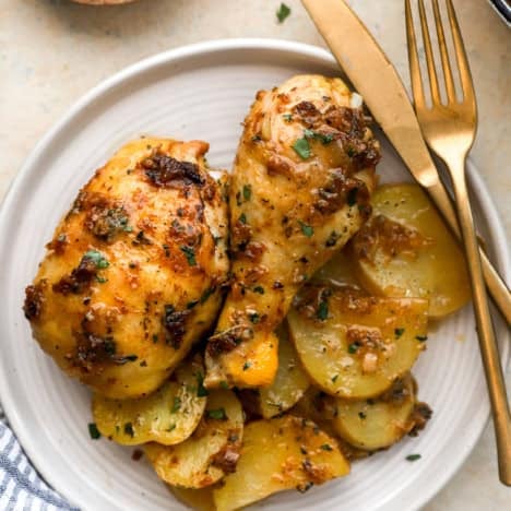 Garlic confit roasted chicken with potatoes on a plate, a knife and fork on the side.