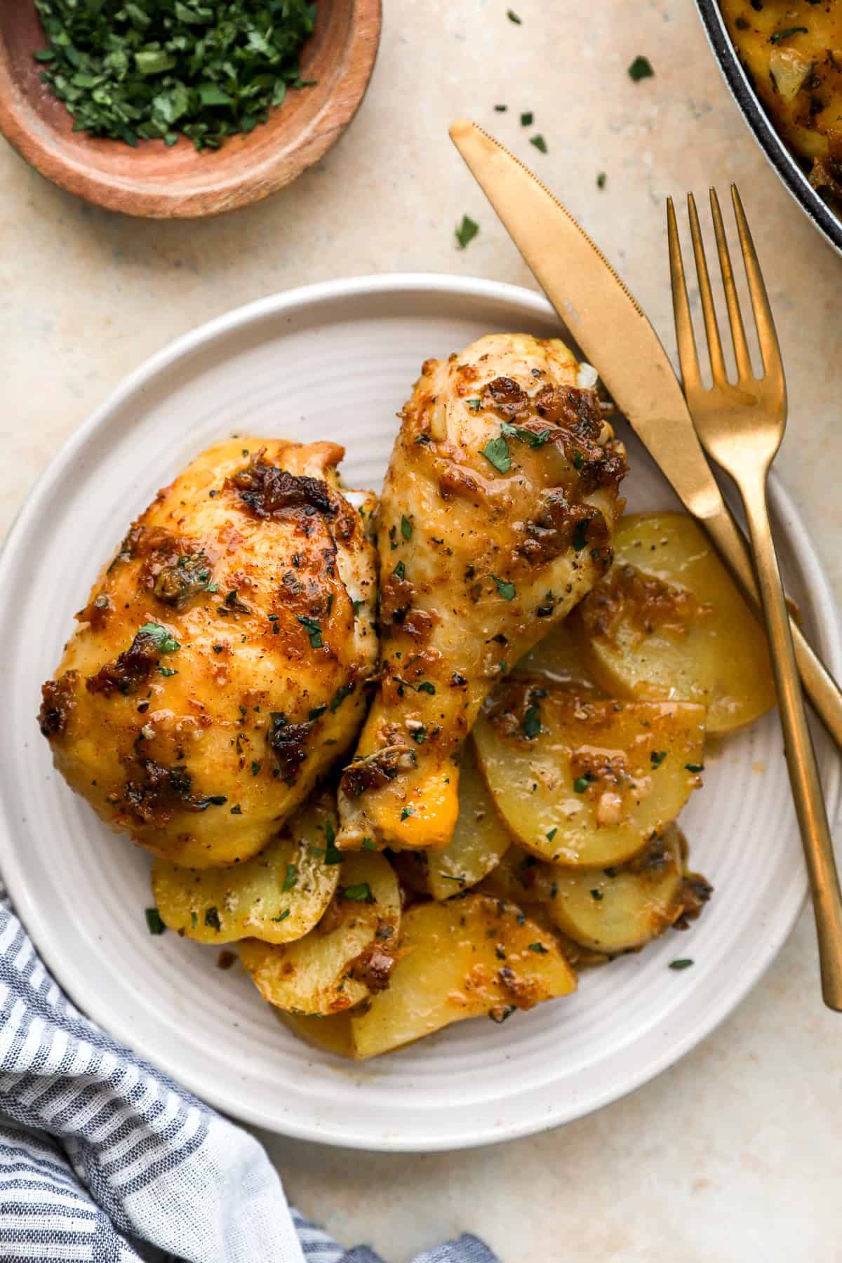 Garlic confit roasted chicken with potatoes on a plate, a knife and fork on the side.