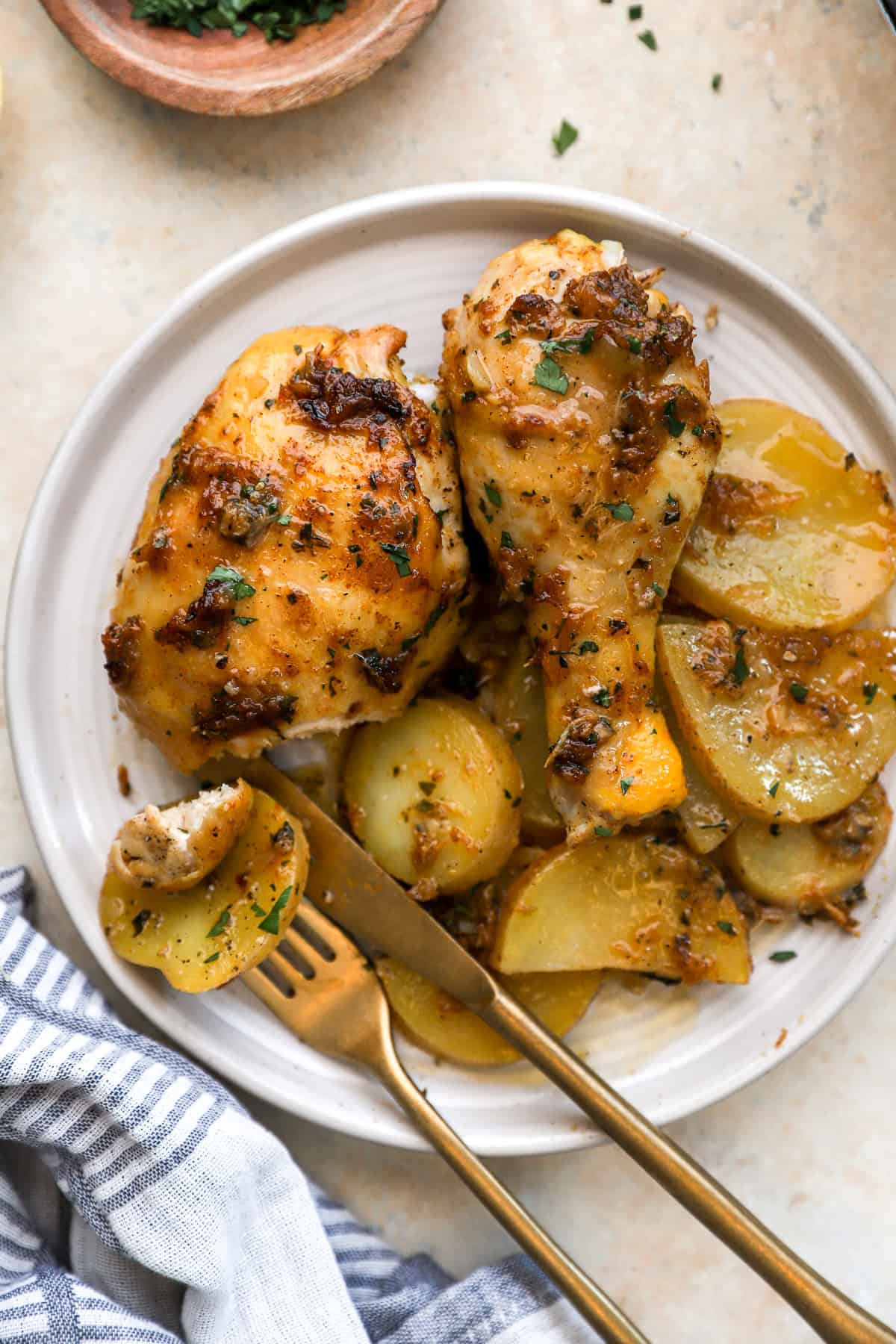 Garlic confit chicken with potatoes on a plate with a fork and knife, the fork spearing a potato.