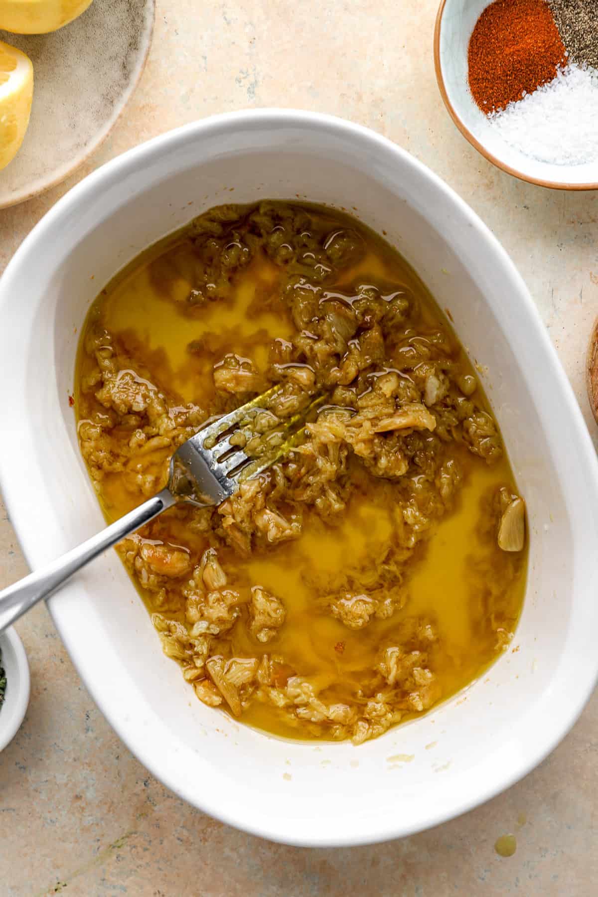 A fork smashing roasted garlic cloves to make garlic confit.