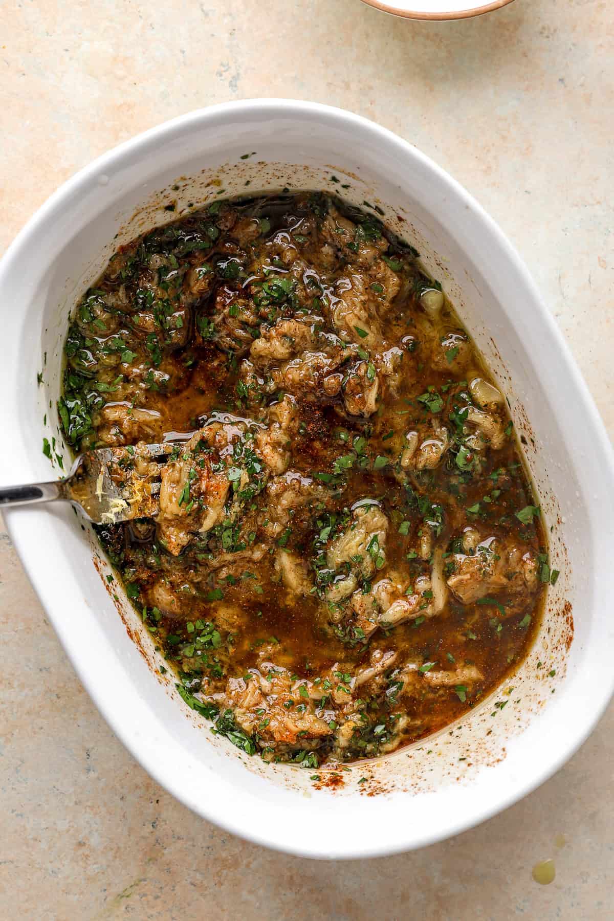 Wet rub ingredients being whisked with garlic confit in a baking dish.
