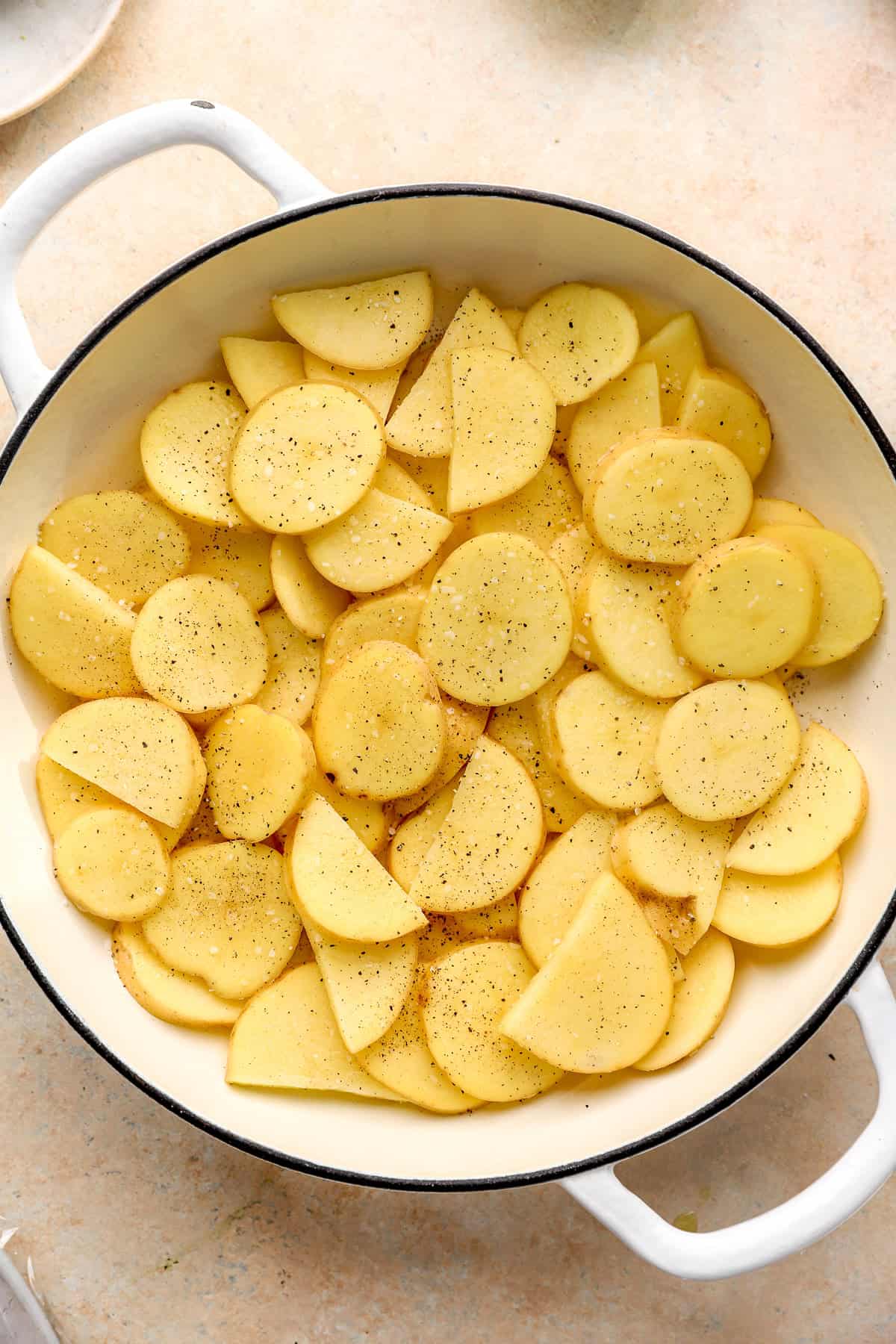 Seasoned potato slices in an even layer in a baking pan.