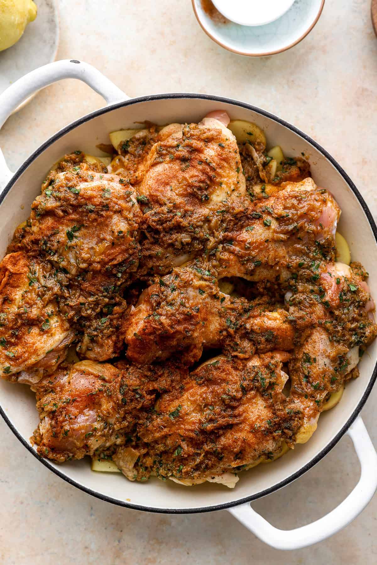 Chicken coated with garlic confit in a braising pan on top of potatoes.