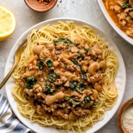 Sausage butter beans served over angel hair pasta on a plate.