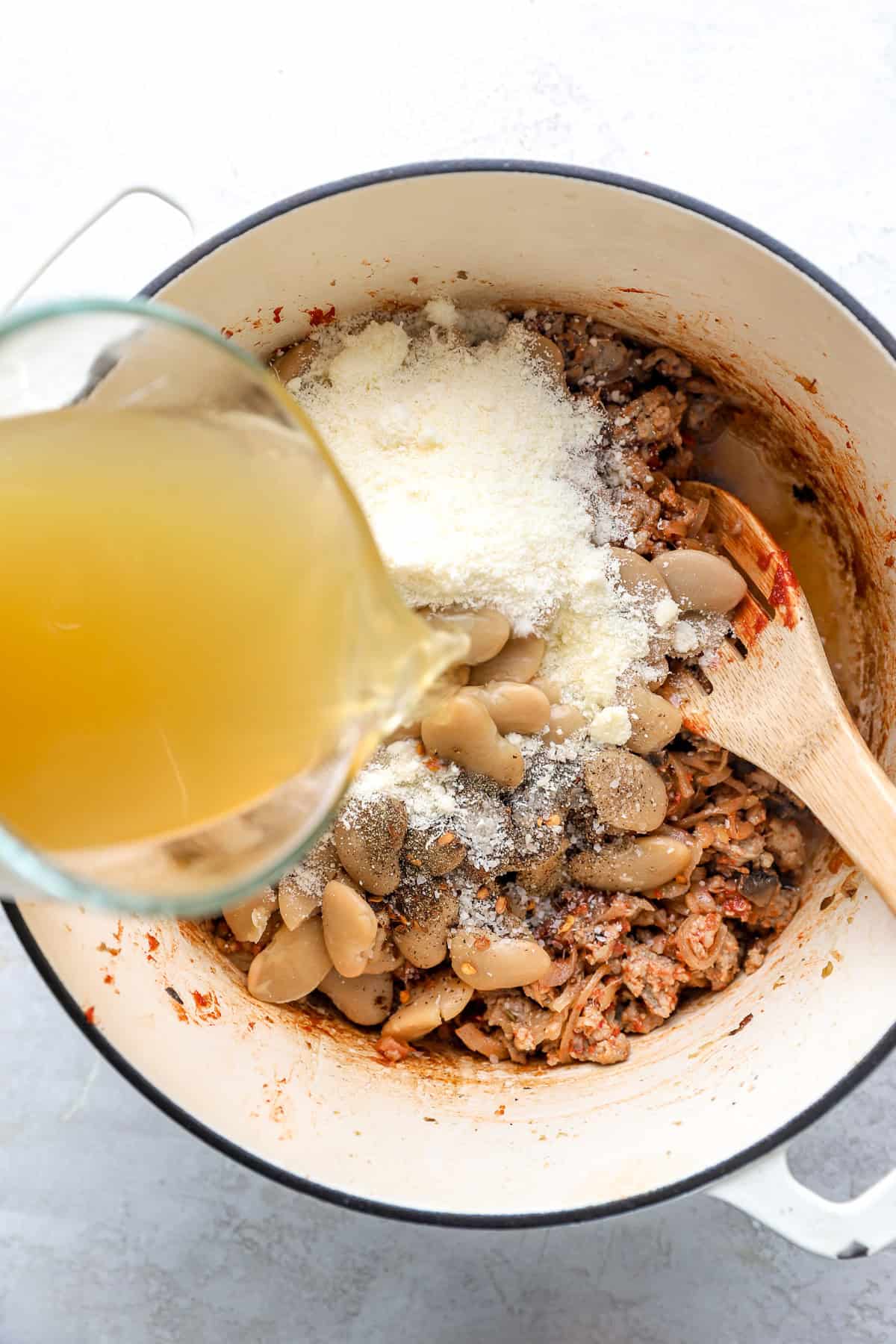 Broth and Parmesan being added to a pot of butter beans. 