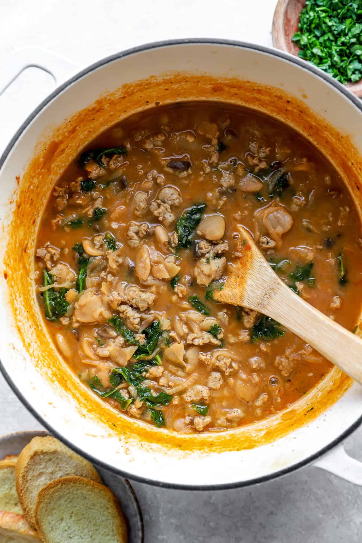 A pot of Parmesan sausage butter beans with a wooden spoon sticking out. 