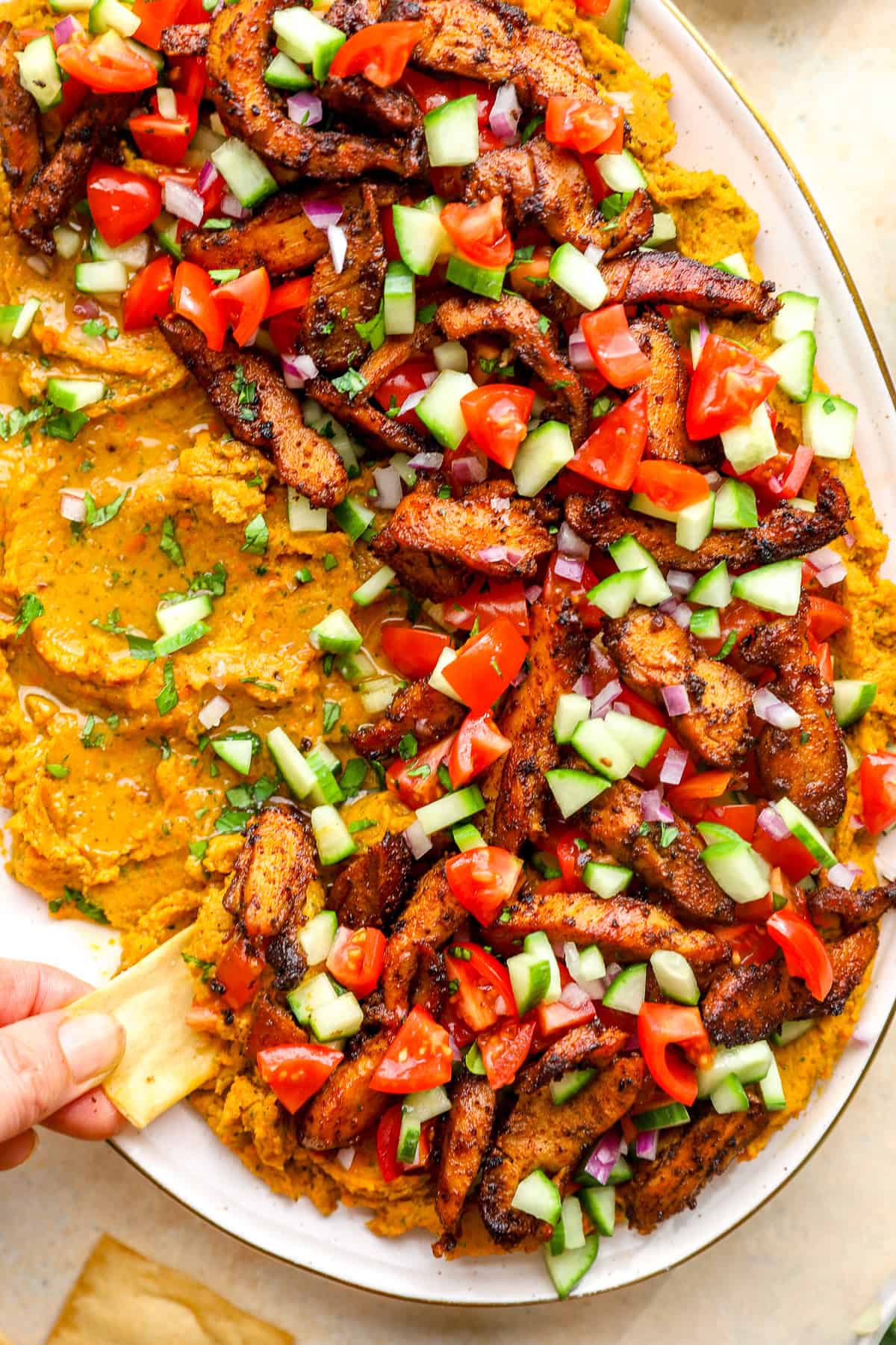 A hand dipping a pita chip into loaded hummus dip.