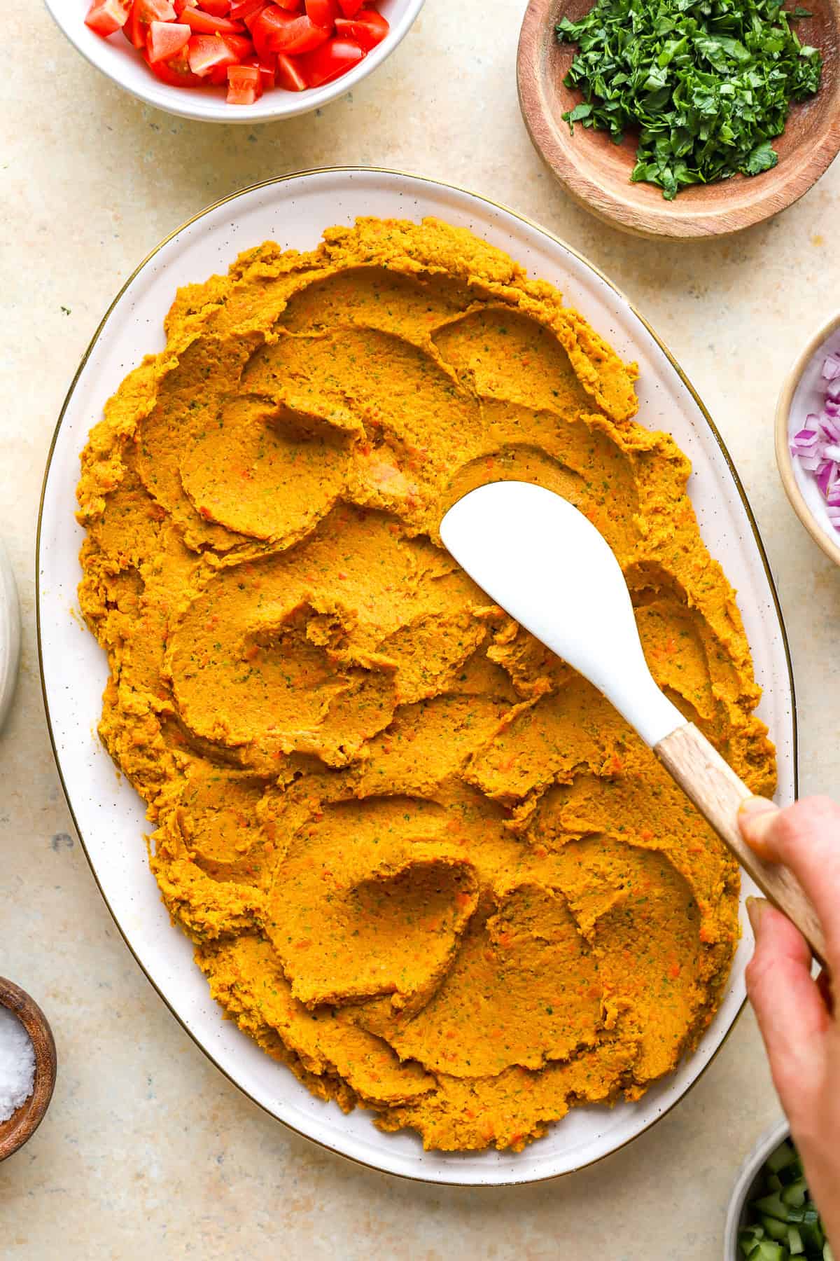 Carrot hummus being spread over a platter.