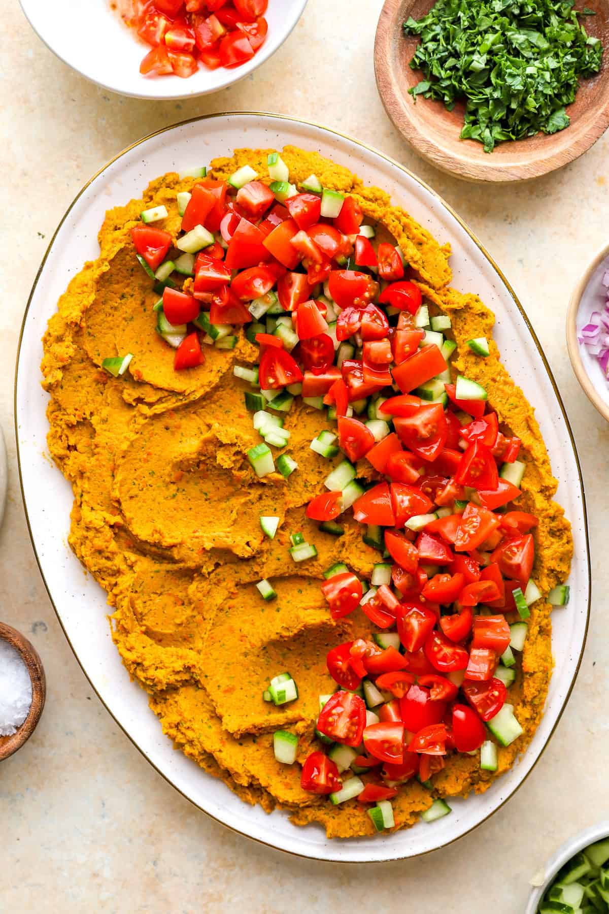 Cucumbers and tomatoes on top of a platter of carrot hummus.