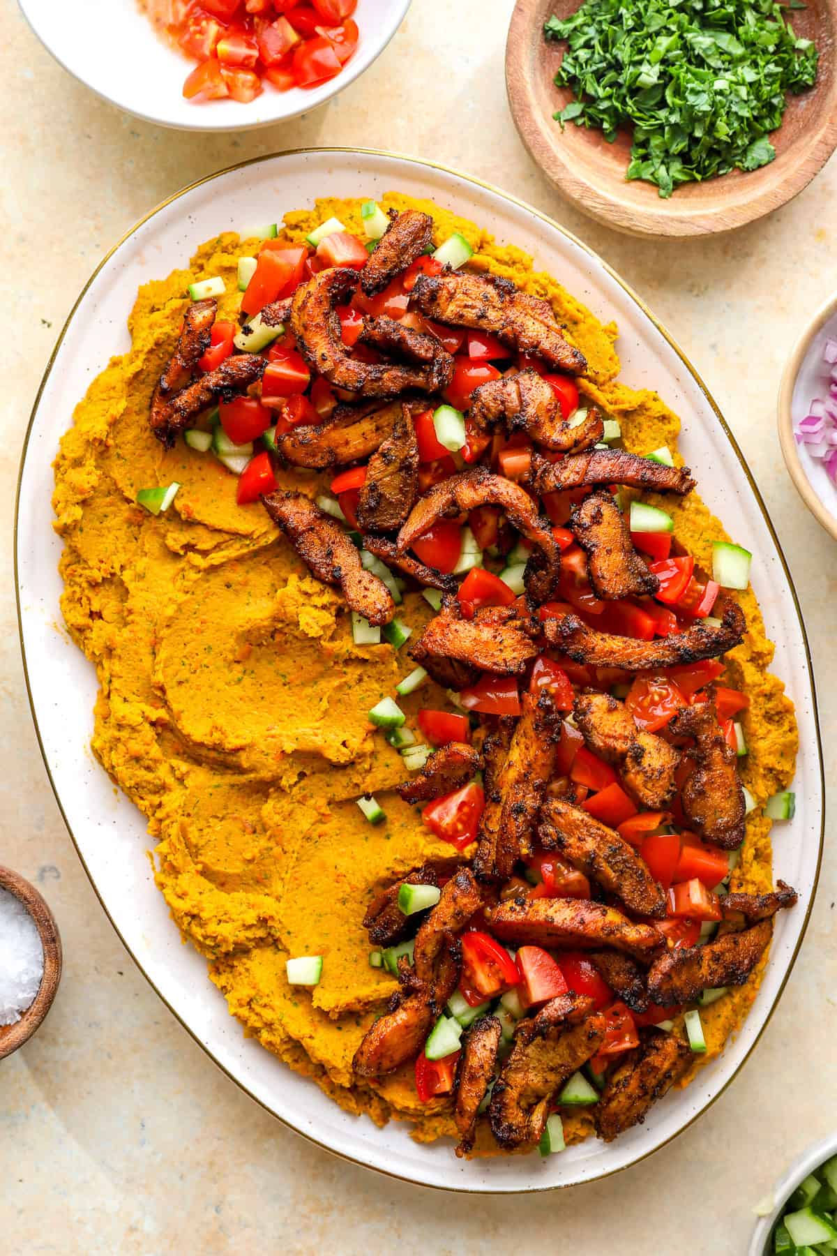 A loaded hummus dip platter with shawarma chicken, tomatoes, and cucumbers.