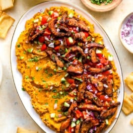 A platter of loaded hummus dip with shawarma chicken, tomatoes, and cucumbers.