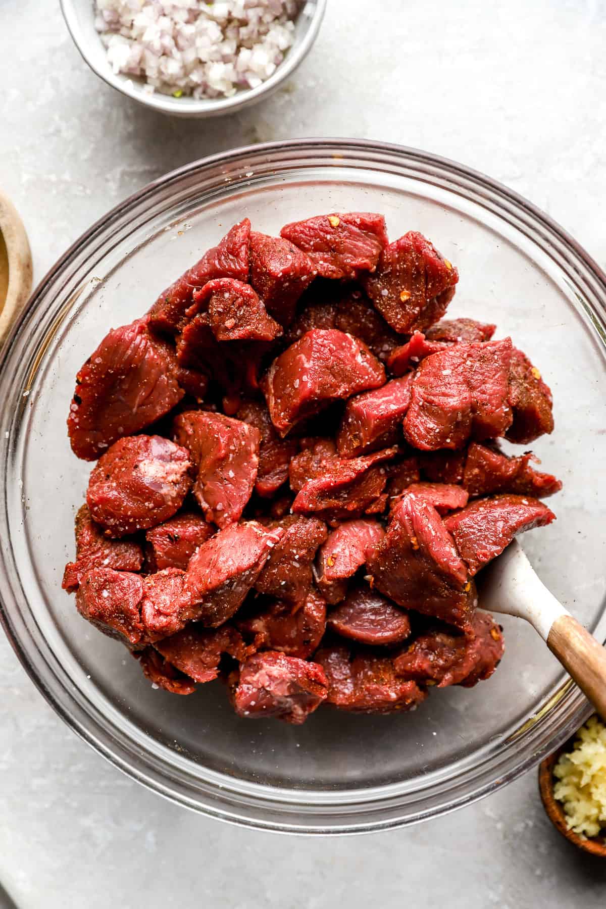 Raw steak bites being tossed with seasonings in a bowl.