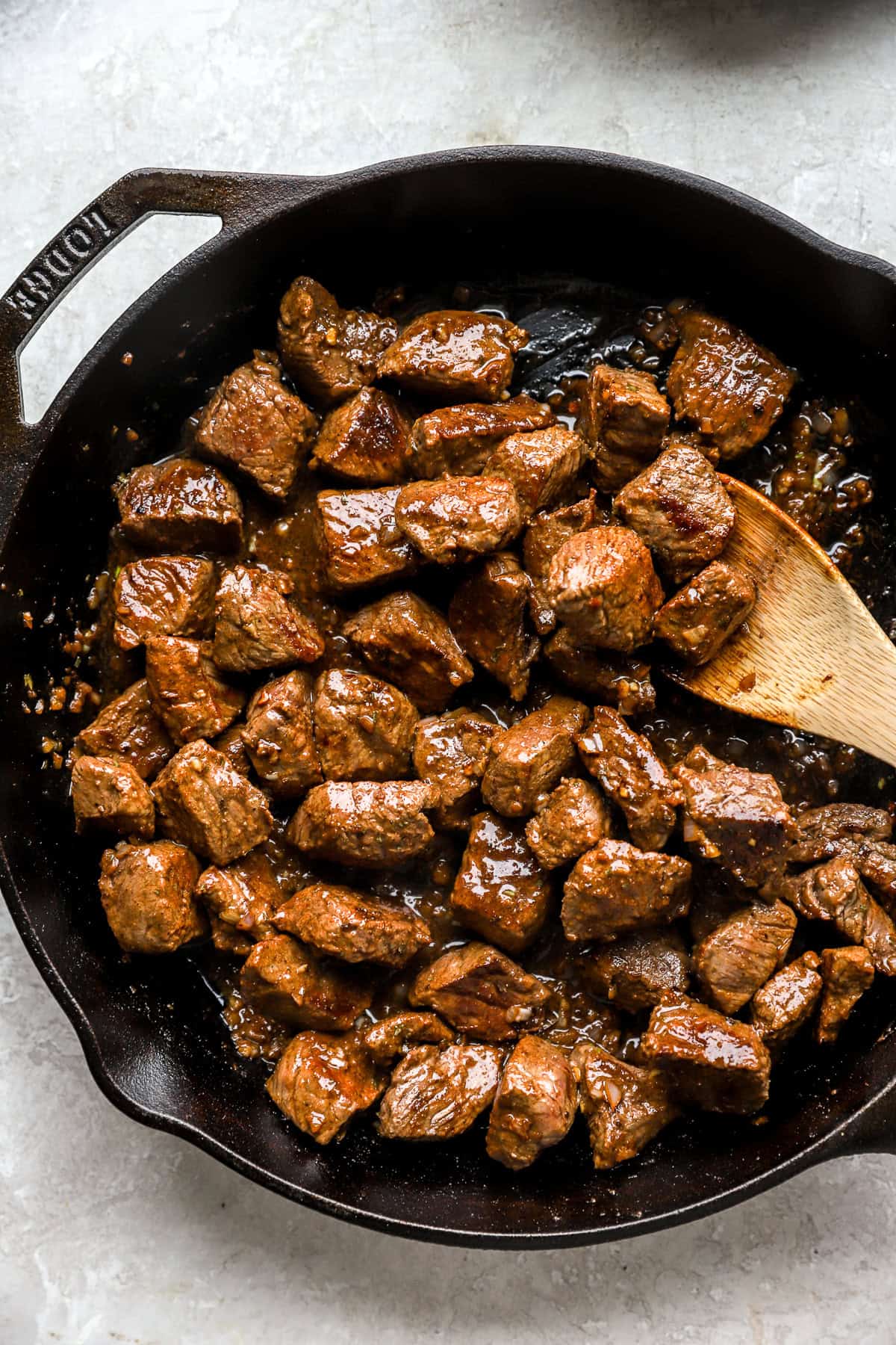 Cooked steak bites being tossed with garlic butter in a cast iron skillet.
