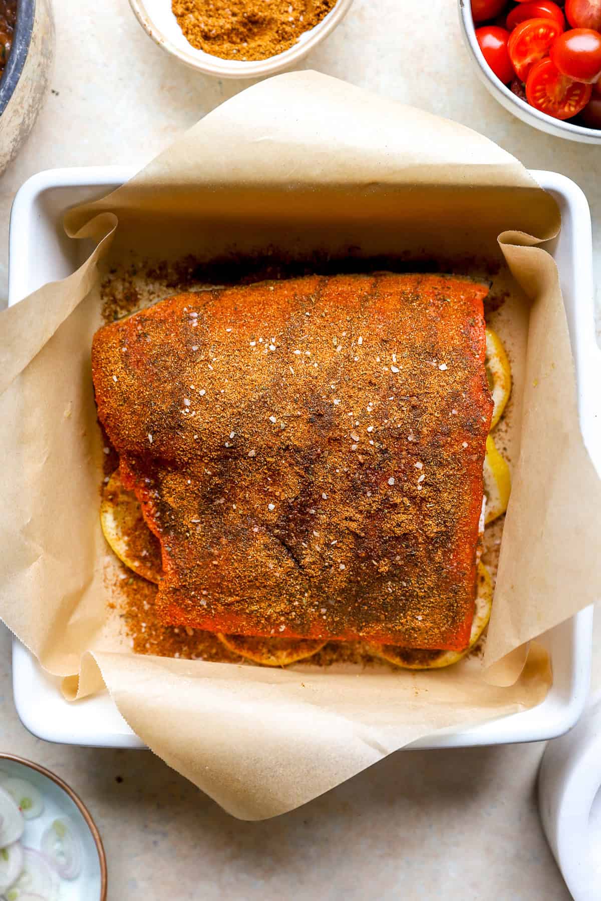 A raw shawarma seasoned salmon filet in a baking dish on top of lemon slices.