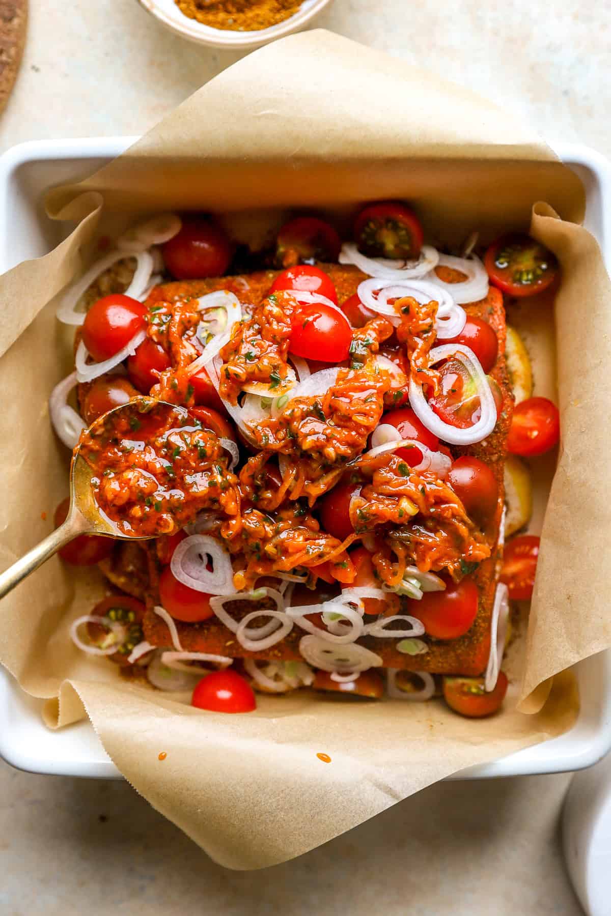 Salmon in a baking sheet being topped with shawarma seasoning and tomato garlic paste.