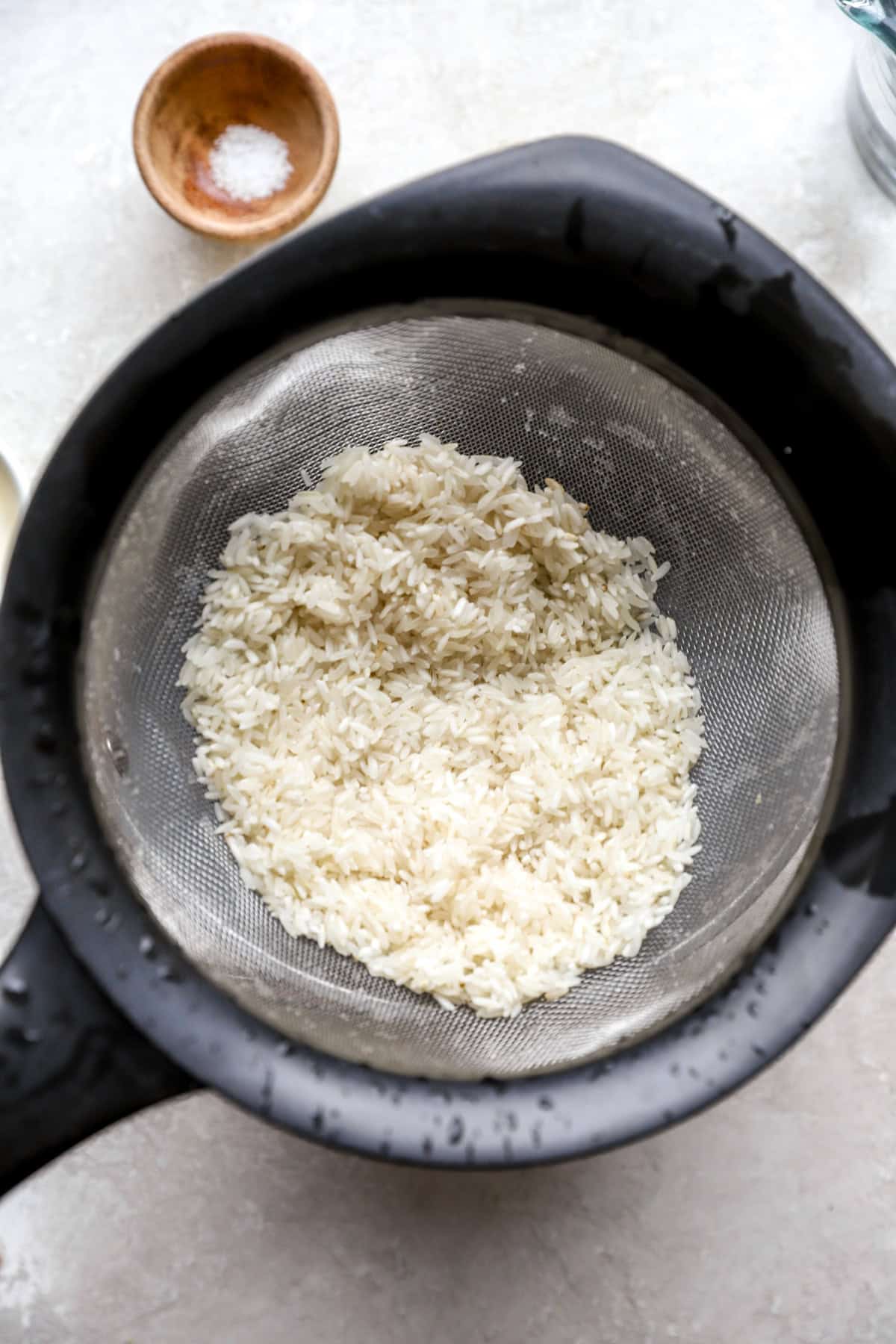 Dry white rice being rinsed in a fine mesh sieve. 
