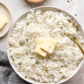 A bowl of cooked white rice topped with two pads of butter.