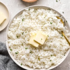 A bowl of cooked white rice topped with two pads of butter.